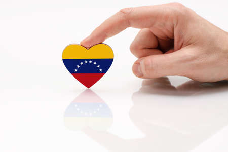 Venezuela flag. Love and respect Venezuela. A man's hand holds a heart in the shape of the Venezuela flag on a white glass surface. The concept of patriotism and pride.の写真素材