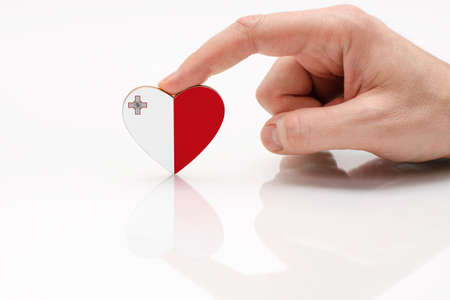 Flag of Malta. Love and respect Malta. A man's hand holds a heart in the shape of the Malta flag on a white glass surface. The concept of Maltese patriotism and pride.の写真素材
