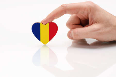 Love and respect Romania. A man's hand holds a heart in the shape of the Romania flag on a white glass surface. The concept of Romanian patriotism and pride.の写真素材