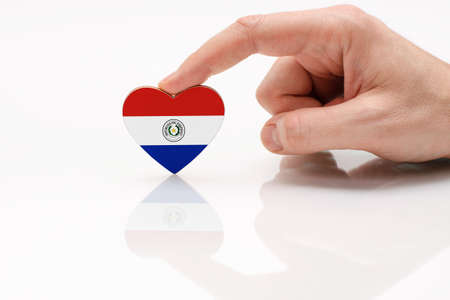Love and respect Paraguay. A man's hand holds a heart in the shape of the Paraguay flag on a white glass surface. The concept of Paraguayan patriotism and pride.の写真素材