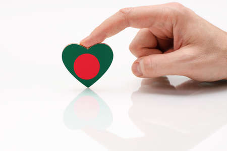 Bangladesh flag in the shape of a heart. Love and respect Bangladesh. A man's hand holds a heart in the shape of the Bangladesh flag on a white glass surface. The concept of patriotism.の写真素材