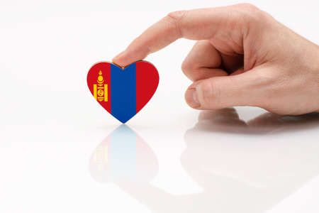 Love and respect Mongolia. A man's hand holds a heart in the shape of the Mongolia flag on a white glass surface. The concept of Mongolian patriotism and pride.の写真素材