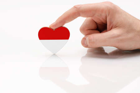 Love and respect Indonesia. A man's hand holds a heart in the shape of the Indonesia flag on a white glass surface. The concept of Indonesian patriotism and pride.の写真素材