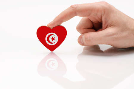 Tunisia flag. Love and respect Tunisia. A man's hand holds a heart in the shape of the Tunis flag on a white glass surface. The concept of patriotism and pride.の写真素材