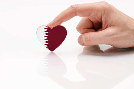 Qatar flag. Love and respect Qatar. A man's hand holds a heart in the shape of the Qatar flag on a white glass surface. The concept of patriotism and pride.の写真素材