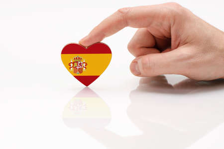 Love and respect Spain. A man's hand holds a heart in the shape of the Spanish flag on a white glass surface. The concept of Spanish patriotism and pride.の写真素材