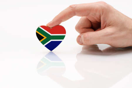 South African flag. Love and respect South Africa. A man's hand holds a heart in the shape of the South Africa flag on a white glass surface. The concept of patriotism and pride.の写真素材