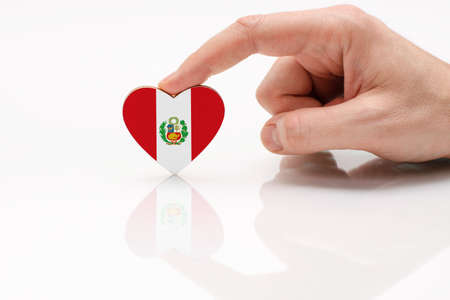 Peru flag. Love and respect Peru. A man's hand holds a heart in the shape of the Peru flag on a white glass surface. The concept of Peruvian patriotism and pride.の写真素材