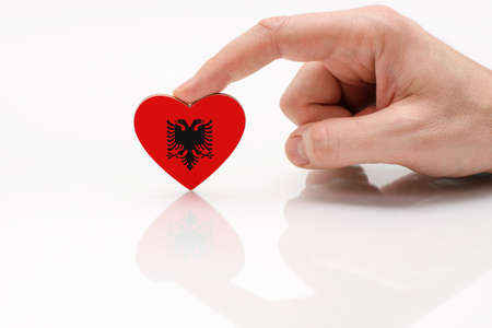 Albania flag. Love and respect Albania. A man's hand holds a heart in the shape of the flag of Albania on a white glass surface. The concept of Albanian patriotism and pride.の写真素材