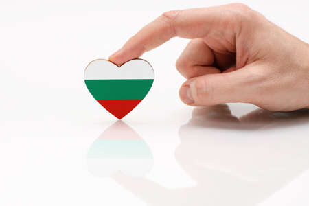 Love and respect Bulgaria. A man's hand holds a heart in the shape of the Bulgaria flag on a white glass surface. The concept of Bulgarian patriotism and pride.の写真素材