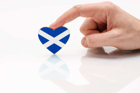 Love and respect Scotland. A man's hand holds a heart in the shape of the Scotland flag on a white glass surface. Scottish patriotism and pride.の写真素材