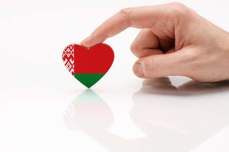 Love and respect Belarus. A man's hand holds a heart in the shape of the Belarus flag on a white glass surface. The concept of Belarusian patriotism and pride.の写真素材