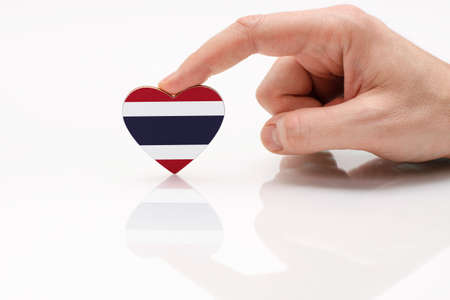 Love and respect Thailand. A man's hand holds a heart in the shape of the Thailand flag on a white glass surface. The concept of Thai patriotism and pride.の写真素材