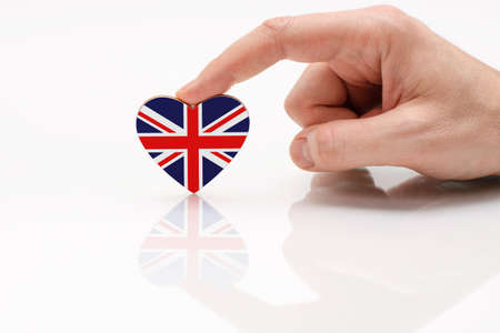 Love and respect Great Britain. A man's hand holds a heart in the shape of the Britain flag on a white glass surface. The concept of British patriotism and pride.の写真素材