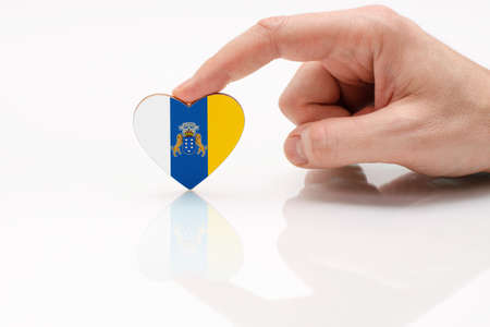Flag of the Canary Islands. Love and respect Canary Islands. A man's hand holds a heart in the shape of the Canary Islands flag on a white glass surface. The concept of patriotism and pride.の写真素材