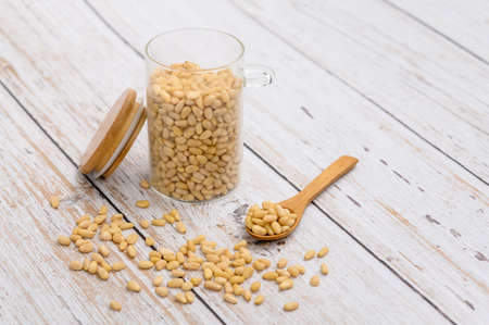 Pine nuts on a wooden light table with a wooden spoon and a glass jar. There is a free space to the right of the frame. Selective focus on a spoonful of nuts.の写真素材