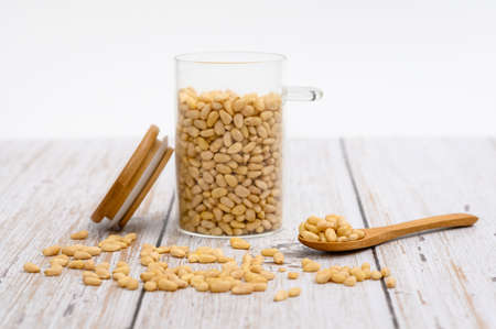 Wooden spoon with pine nuts on the table. Nearby are grains of nuts and a glass cup with nuts. Selective focus on a spoonful of nuts.の写真素材