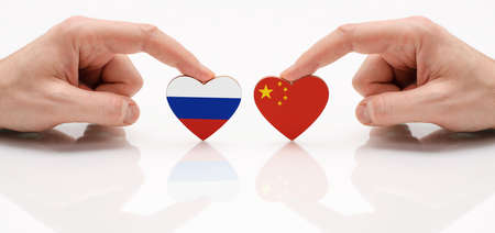 The concept of friendship and diplomatic relations between Russia and the China. Two male hands are holding flags in the shape of a heart on a glass table. The flag of Russia and the Republic of China as a symbol of cooperation and respect.の写真素材