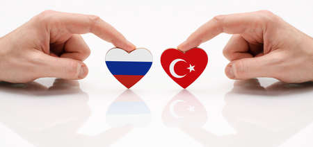 The flag of Russia and Turkey. The concept of friendship and diplomatic relations between Russia and Turkey. Two male hands are holding flags in the shape of a heart on a glassの写真素材