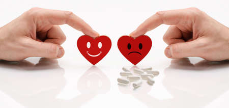 Two hearts with happy and sad emotion. There are pills next to the sad emotion. The concept of comparing a healthy heart and a sick one.の写真素材