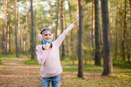 The girl takes off her medical mask in the spring forest and enjoys the fresh air. A girl on a walk rejoices in the spring.の写真素材