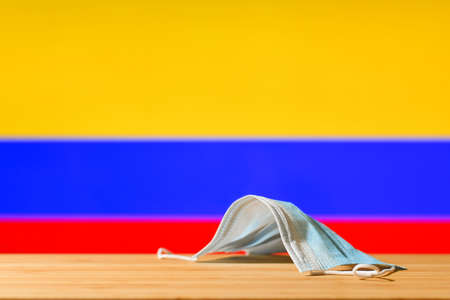 A medical mask lies on the table against the background of the flag of Colombia. The concept of a mandatory mask regime for residents of the country and tourists in Colombia during a pandemic.の写真素材