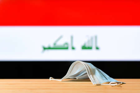 A medical mask lies on the table against the background of the flag of Iraq. The concept of a mandatory mask regime for residents of the country and tourists in Iraq during a pandemic.の写真素材