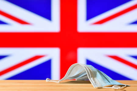 A medical mask lies on the table against the background of the flag of Great Britain. The concept of a mandatory mask regime for residents of the country and tourists in Great Britain during a pandemic.の写真素材