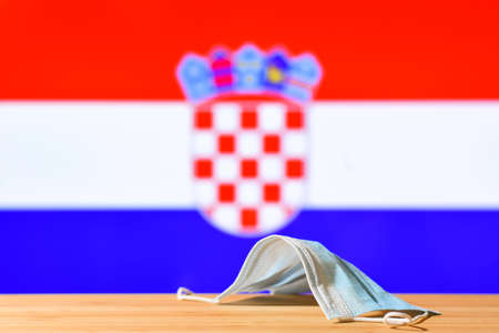 A medical mask lies on the table against the background of the flag of Croatia. The concept of a mandatory mask regime for residents of the country and tourists in Croatia during a pandemic.の写真素材