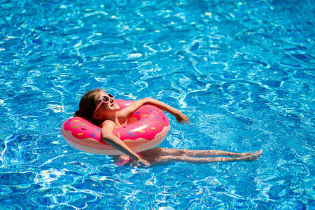 Attractive cheerful girl swims in the pool on a pink rubber ring. Portrait of a happy girl while swimming in the poolの写真素材