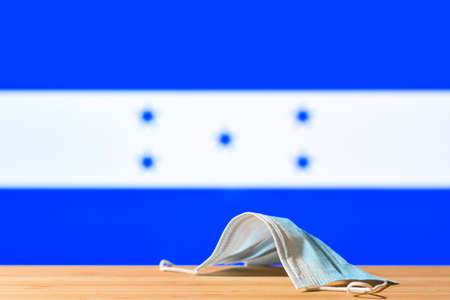 A medical mask lies on the table against the background of the flag of Honduras. The concept of a mandatory mask regime for residents of the country and tourists in Honduras during a pandemic.の写真素材
