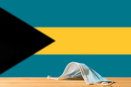 A medical mask lies on the table against the background of the flag of Bahamas. The concept of a mandatory mask regime for residents of the country and tourists in Bahamas during a pandemic.の写真素材