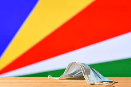 A medical mask lies on the table against the background of the flag of Seychelles. The concept of a mandatory mask regime for residents of the country and tourists in Seychelles during a pandemic.の写真素材