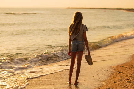 A girl stands on the seashore and looks at the sunset.の写真素材