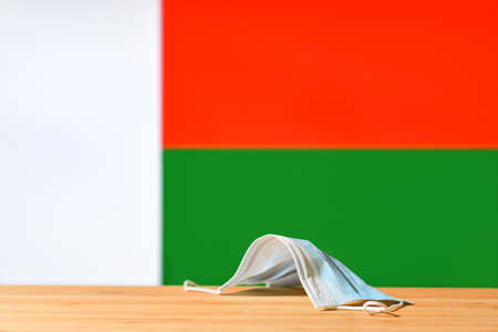 A medical mask lies on the table against the background of the flag of Madagascar. The concept of a mandatory mask regime for residents of the country and tourists in Madagascar during a pandemic.の写真素材
