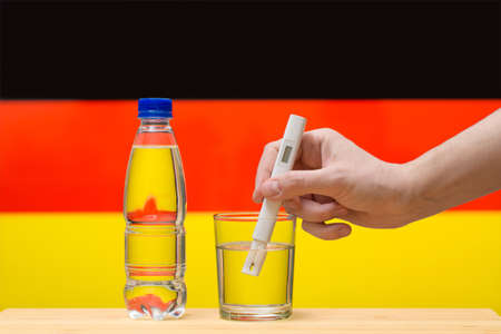 A hand with a water tester makes a measurement in a glass of clear water against the background of the flag of Germany. Test and assessment of drinking water supplies in Germany.の写真素材