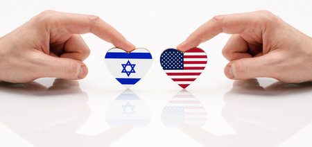 The concept of friendship and diplomatic relations between Israel and USA. Two male hands are holding flags in the shape of a heart on a glass table. The flag of Israel and USA as a symbol of cooperation and respect.の写真素材