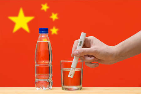 A hand with a water tester makes a measurement in a glass of clear water against the background of the flag of China. Test and assessment of drinking water supplies in China.の写真素材