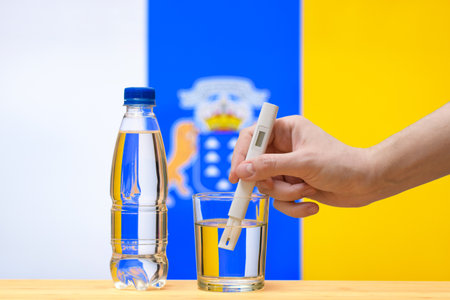 A hand with a water tester makes a measurement in a glass of clear water against the background of the flag of Canary Islands. Test and assessment of drinking water supplies in Canary Islands.の写真素材