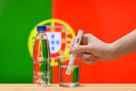 A hand with a water tester makes a measurement in a glass of clear water against the background of the flag of Portugal. Test and assessment of drinking water supplies in Portugal.の写真素材