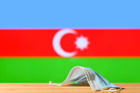 A medical mask lies on the table against the background of the flag of Azerbaijan. The concept of a mandatory mask regime for residents of the country and tourists in Azerbaijan during a pandemic.の写真素材