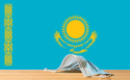 A medical mask lies on the table against the background of the flag of Kazakhstan. The concept of a mandatory mask regime for residents of the country and tourists in Kazakhstan during a pandemic.の写真素材