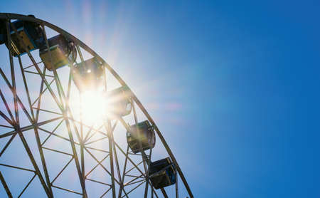 Part of the Ferris wheel against the background of the sky and the bright sun. Free space on the right for text.の写真素材