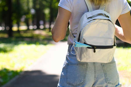 A medical mask sticks out of the backpack of a girl on a walk in the park. Focusing on the mask.の写真素材