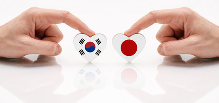 The concept of friendship and diplomatic relations between South Korea and Japan. Two hands are holding flags in the shape of a heart on a glass table. The flag of South Korea and Japan as a symbol of cooperation and respect.の写真素材
