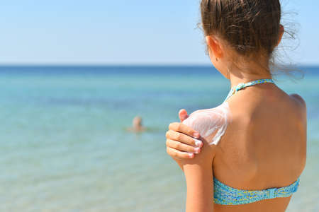 girl on the beach smears sunscreen on her shoulder and looks at the sea. Selective focus on the shoulder with cream.の写真素材