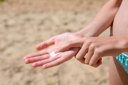 White sunscreen in a child's hand on the background of a sandy beach. Sun protection for children on vacationの写真素材