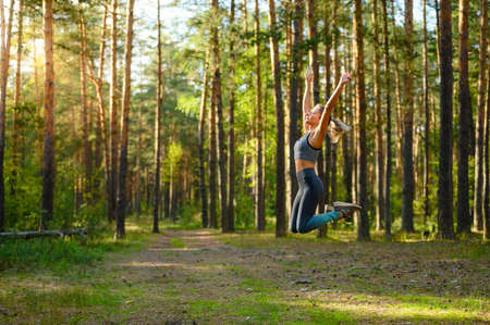 A sportive girl jumps with her hands high in a pine forest. Selective focusing.の写真素材