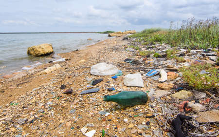 Very dirty seashore. Environmental disaster from human negligence. Selective focus on the green bottle.の写真素材
