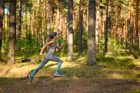 Girl jogging in a pine forest. Active lifestyle and outdoor sports.の写真素材